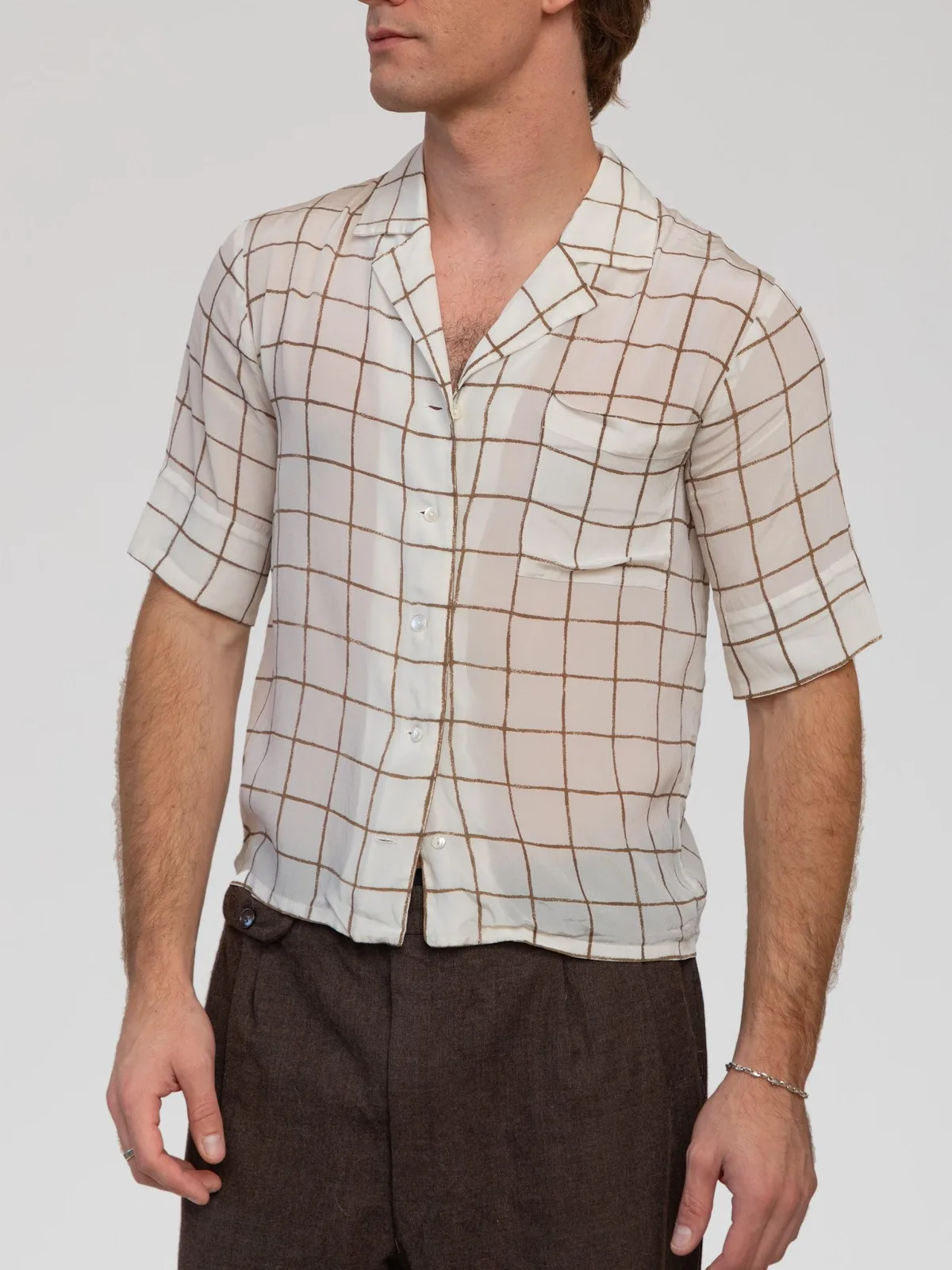 Vintage Christian Dior short-sleeve camp shirt in off-white featuring a brown windowpane grid check pattern. Crafted from lightweight, semi-sheer woven silk with an open relaxed collar, a front patch pocket at the chest, pearlized front buttons, and a straight hemline.