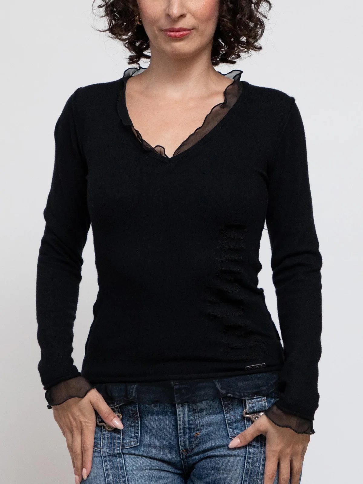 This black long-sleeve knit top features a V-neckline with mesh ruffle trim, sheer mesh cuffs, vertical side ruching along the left waist, and a layered mesh hemline.