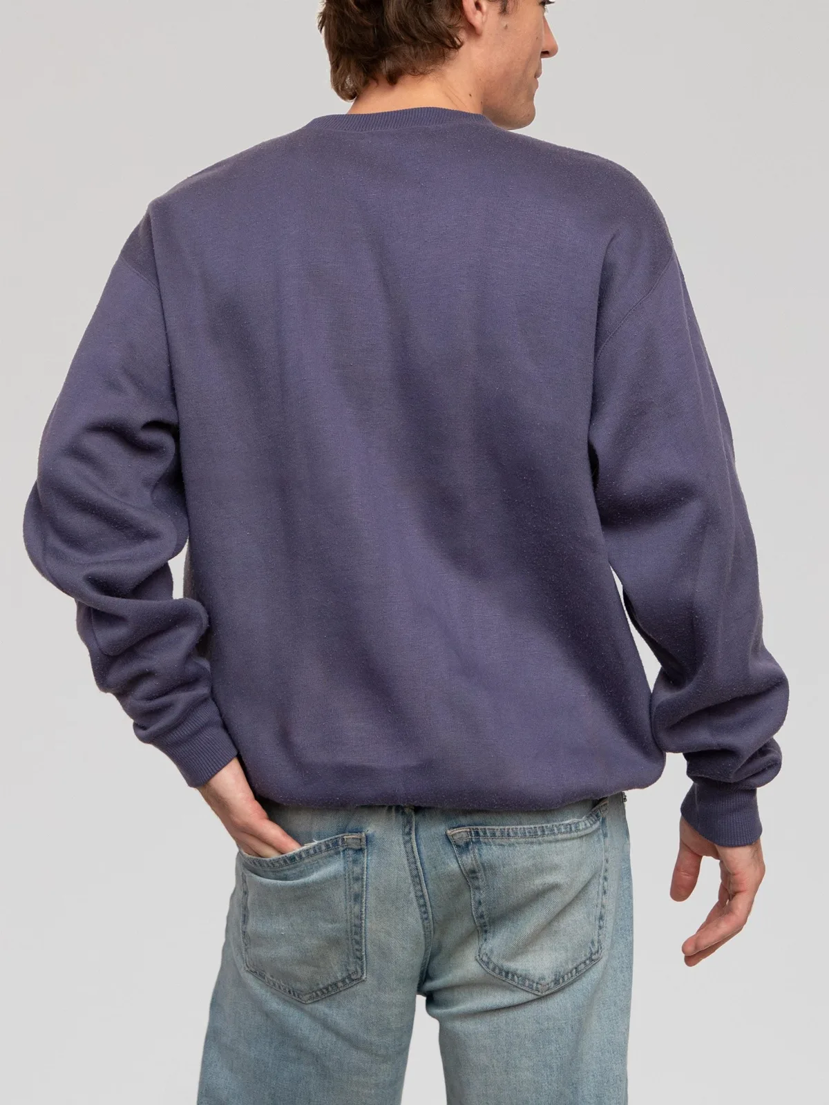 Vintage Gianni Valentino long-sleeve fleece sweatshirt in a muted slate blue hue. Features an embroidered gold "GV" logo emblem and black "GIANNI VALENTINO ITALY" branding across the chest. Designed with a relaxed, slouchy silhouette, dropped shoulders, a ribbed crewneck collar, and ribbed cuffs and hem.